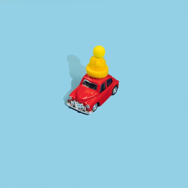 Red toy car in yellow winter cap on blue background