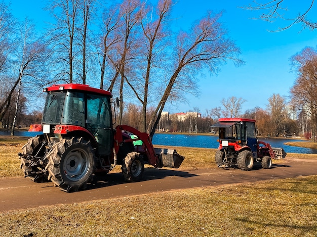 Red tractors trucks in spring city park. Cleaning. Early spring. Works. Sunny spring day.