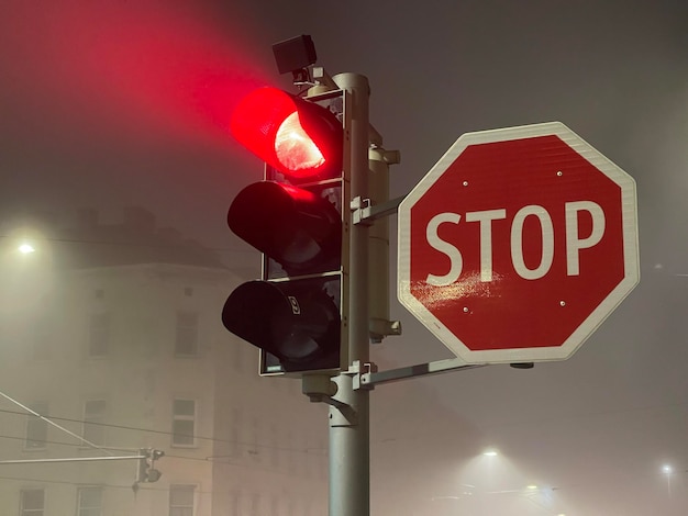 Red traffic lights glowing in the fog near big stop sign