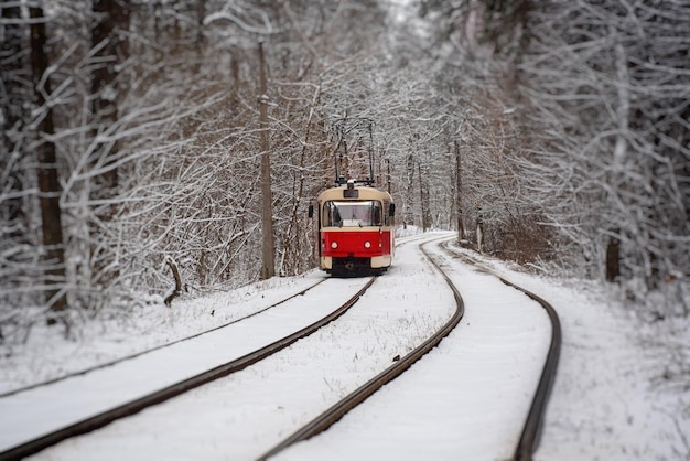 Red tram moving on the rails in the winter snowy forest seasonal background