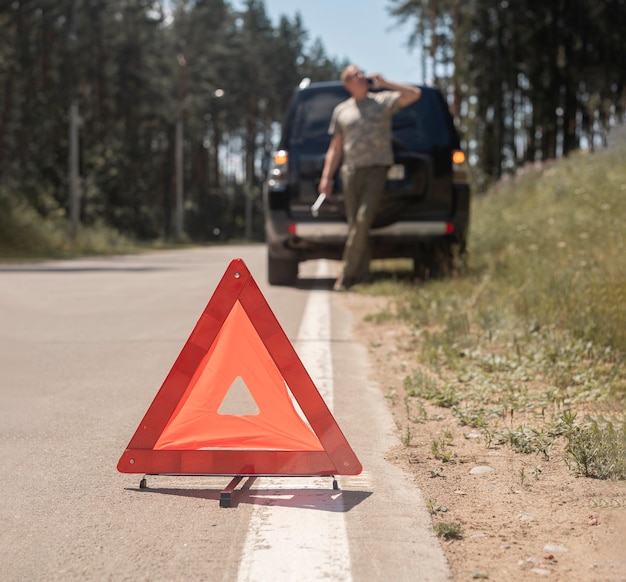 Фото Предупреждающий знак красного треугольника на дороге после поломки автомобиля и размытого водителя, говорящего по мобильному телефону ...
