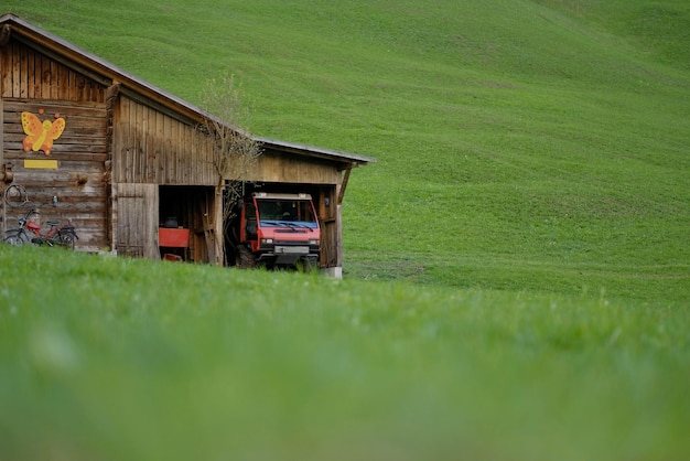 A red truck is parked in a barn with a green field in the background.