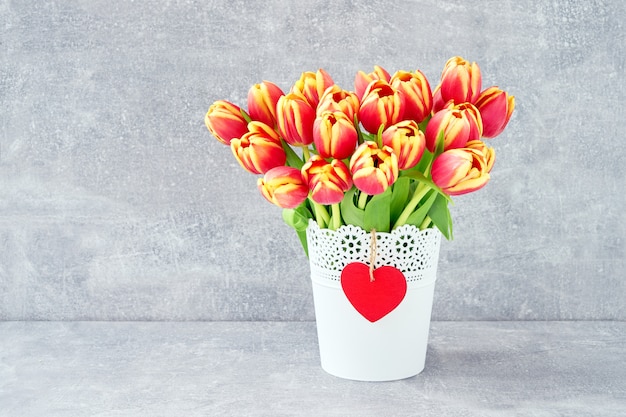 Mazzo rosso dei tulipani in vaso di fiori bianco su fondo grigio. sfondo di vacanza, copia spazio.