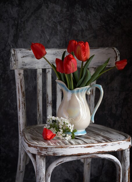 Red tulips bouquet in white vase on vintage chair.