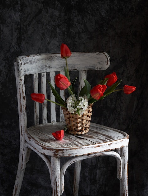 Red tulips bouquet in white vase on vintage chair