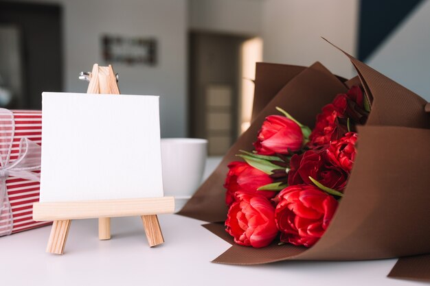 Red tulips bouquet with coffee cup. Empty white frame. Pink gift box. Greeting card concept