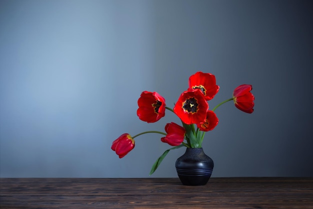 Red tulips in dark ceramic vase on wooden table