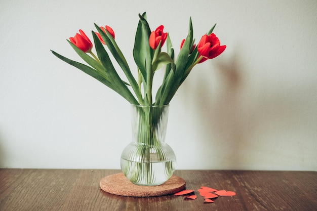 Red tulips flower bouquet in glass vase on table empty copy space.Fresh flowers on wooden background