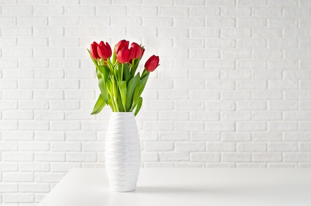Фото Красные тюльпаны в белой вазе на фоне белого кирпича