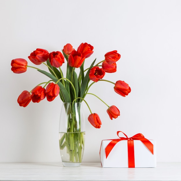 Red tulips in a vase and gift on the table on white.