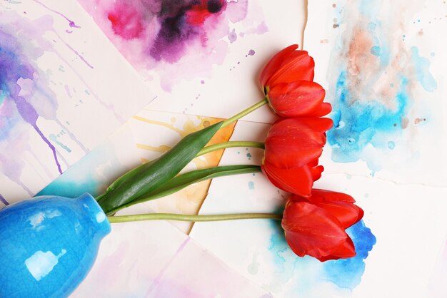 red tulips in vase on watercolor sketches background top view