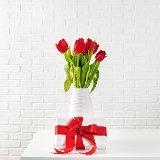 Red tulips in white vase with gift box with red ribbon