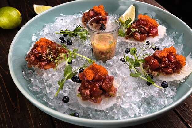 Red tuna tartare in ice on the green plate with lime and blueberries