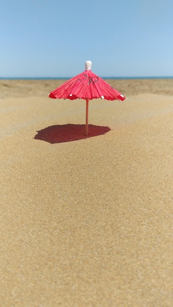 Photo a red umbrella in the sand with the ocean in the background.