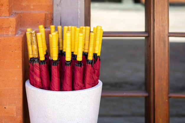 Red umbrellas with a yellow handle is placed in a ceramic pot outdoors.