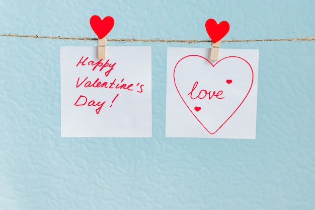 Red Valentine's love hearts pin hanging on natural cord against blue background. drawn heart on paper piece.