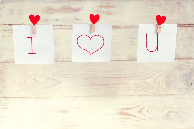 Red Valentine's love hearts pins hanging on natural cord against white wooden background. I love you inscription on paper pieces.