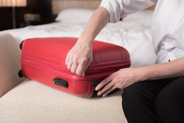 赤いvalise。ソファの上に横たわっている現代の大きな赤いvaliseとそれに触れる年配の女性