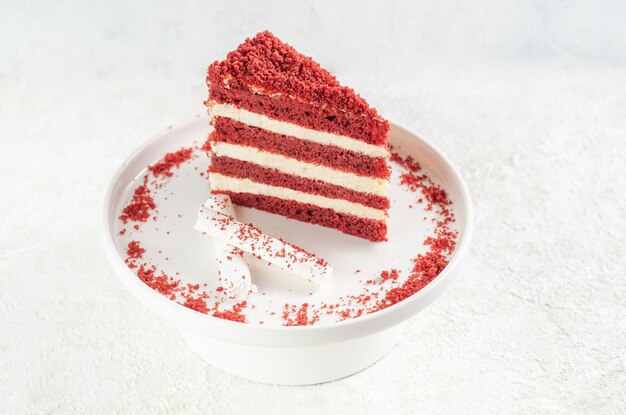 Red velvet cake. Piece on a white plate. Decorated with crumb and marshmallows. Light background.