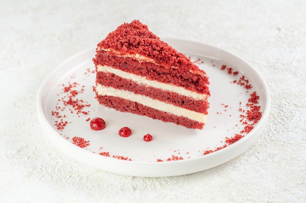 Red velvet cake. Piece on a white plate. Garnished with crumbs and cranberry sauce. Light background.