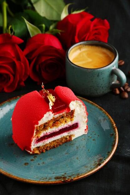 Torta di velluto rosso sul piatto con una tazza di caffè e rose