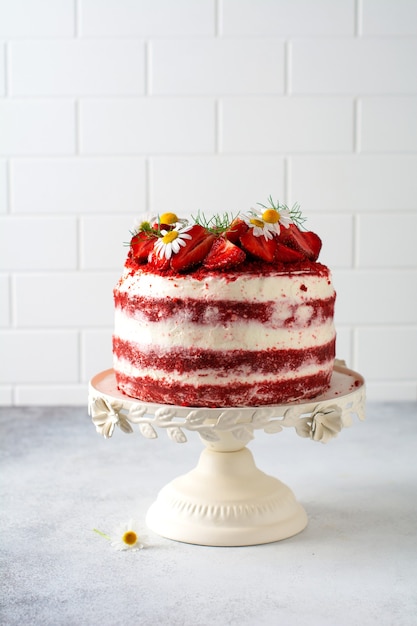 Photo red velvet cake with strawberry, whipped cream and bouquet of daisies on white board on gray background. valentines day, wedding dessert or birthday party. bakery, confectionery concept. copy space.