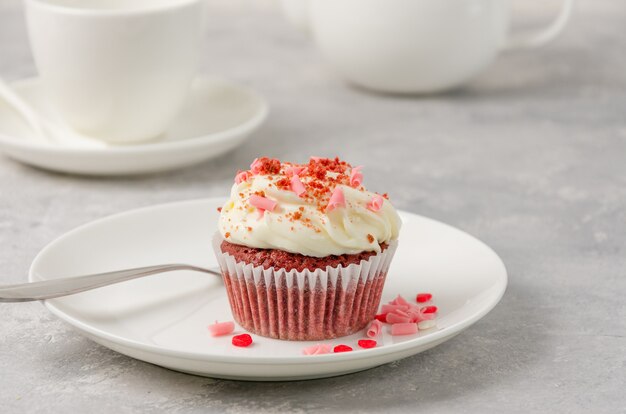 Red velvet cupcakes with cream cheese icing are decorated for Valentine's Day on a white plate on a gray background. Copy space.