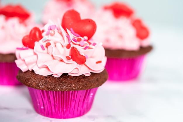 Red velvet cupcakes with pink Italian buttercream frosting and decorates with heart and kiss shaped red chocolates.