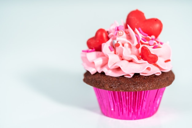 Red velvet cupcakes with pink Italian buttercream frosting and decorates with heart and kiss shaped red chocolates.