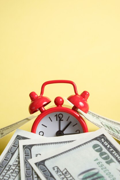 Photo red vintage clock with many one hundred us dollar bills on yellow