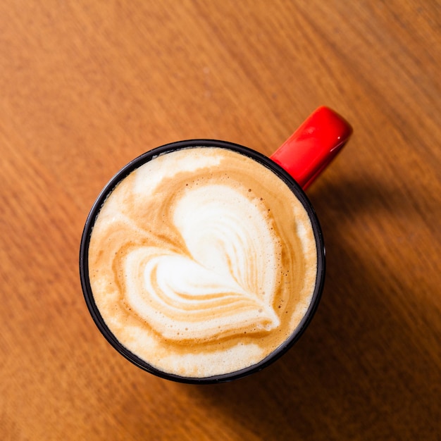 Красная винтажная чашка кофе латте-арт на деревянном столе в вид сверху