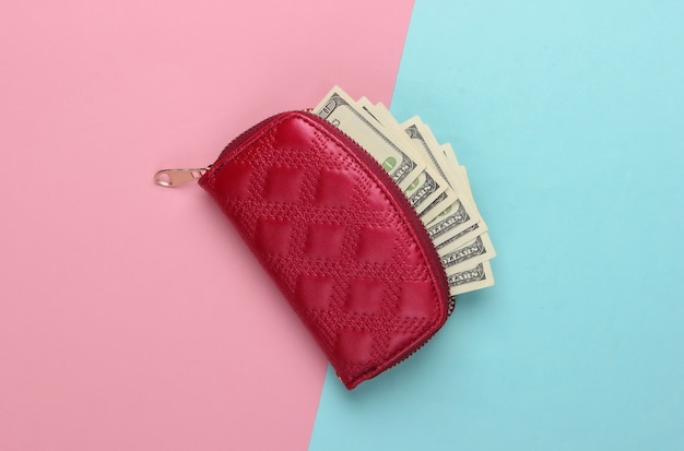 Red wallet with hundred dollar bills on a blue-pink pastel.