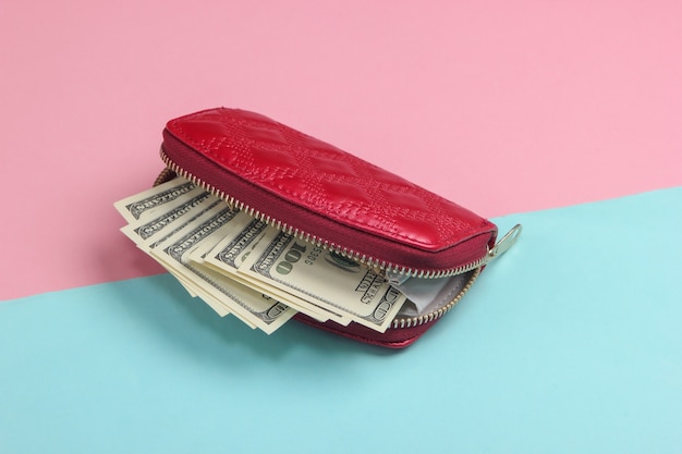 Red wallet with hundred dollar bills on a blue-pink pastel.