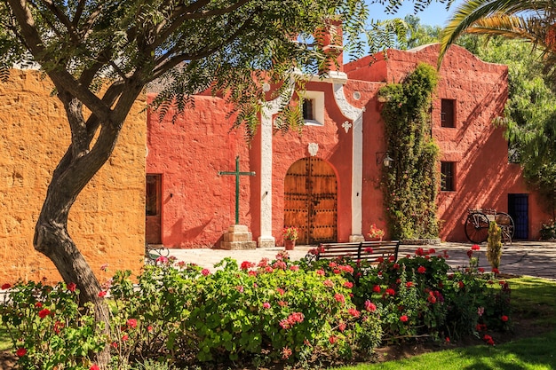 Red walls and gate of Spanish catholic chapel with trees and flowers at front Arequipa Peru