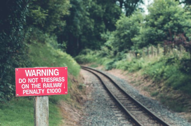 Photo red warning sign by railroad track against trees