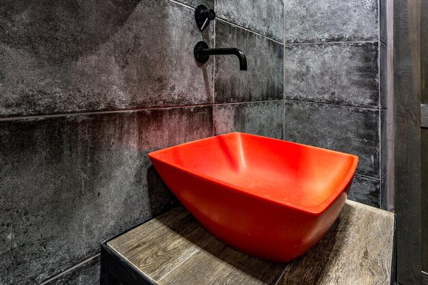 Red washbasin with faucet in expensive loft bathroom in elite sport bar on black brick wall background