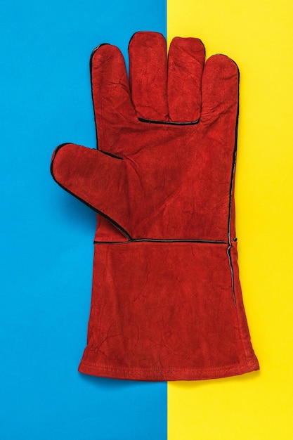 Red welder's glove closeup on a yellow and blue background