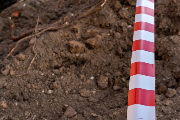 Красно-белая заграждающая лента защищает опасное место Лента предупреждающая сигнализирует об опасности нахождения на территории строительной площадки Вырытые траншеи для прокладки новых труб