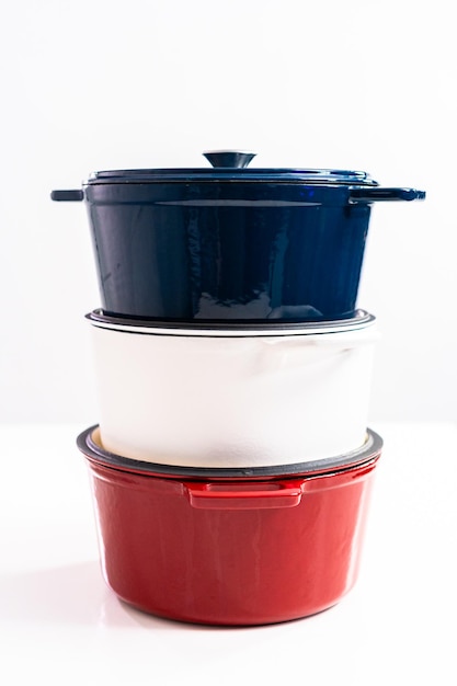 Red, white and blue enameled cast iron covered round dutch ovens on a whjite background.