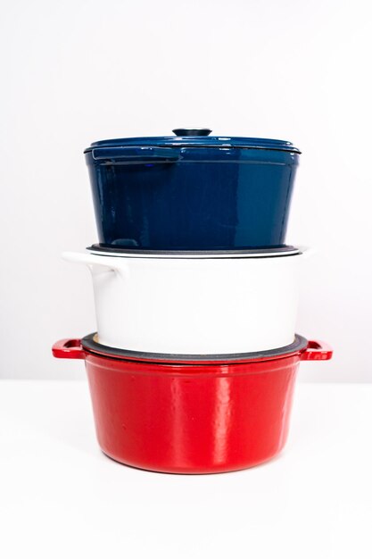 Red, white and blue enameled cast iron covered round dutch ovens on a whjite background.