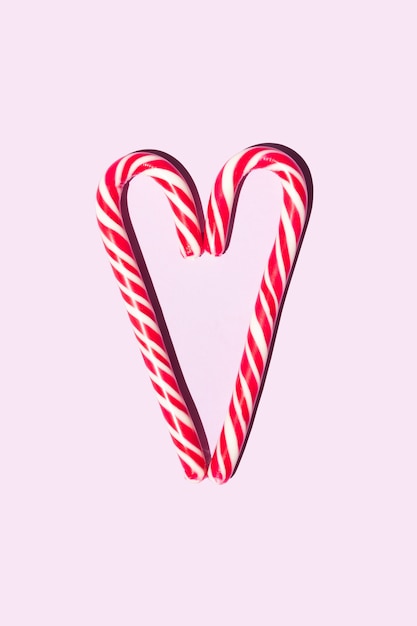 Red and white christmas candy staffs in the form of a heart on a pink background