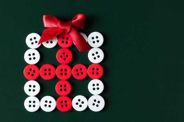 緑色の背景に縫うボタンで作られた赤/白のクリスマスのギフトボックス