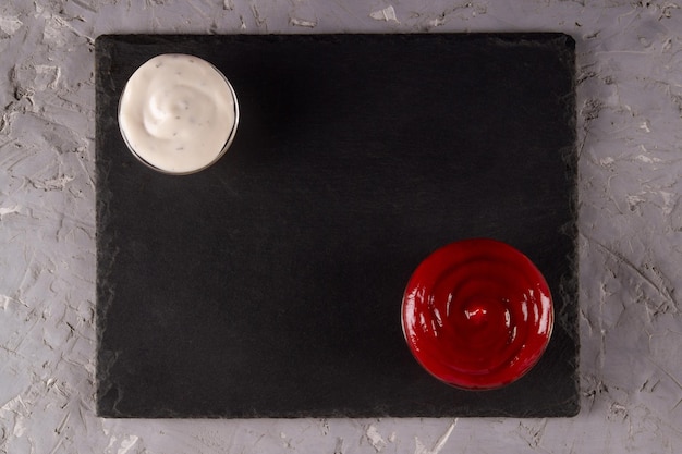 Red and white dipping sauces on black slate serving board with blank space