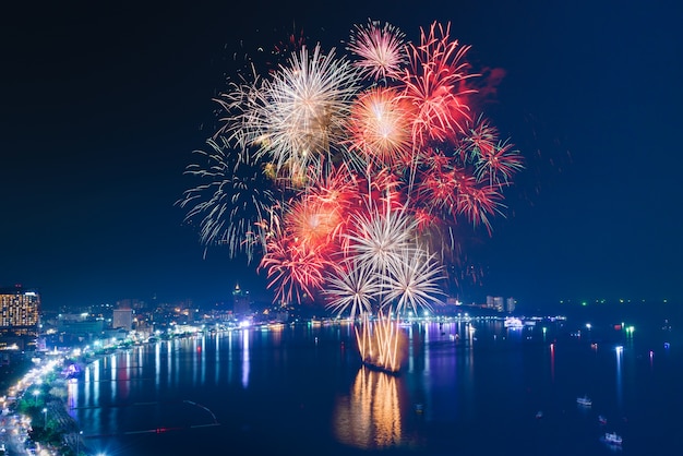 Foto fuochi d'artificio rosso, bianco e oro ver il mare con sfondo blu cielo crepuscolare e vista sulla città