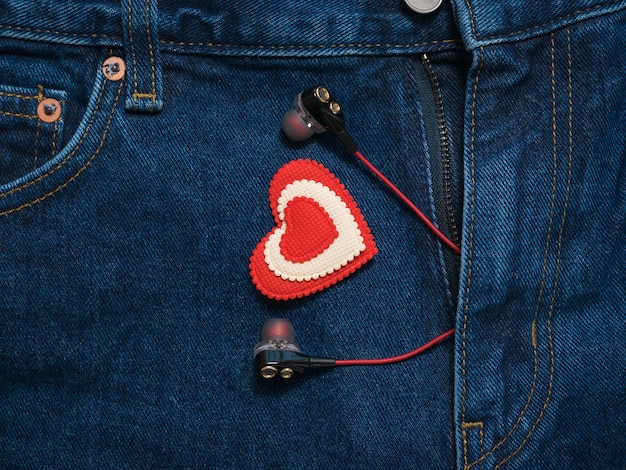 Красно-белое сердце с наушниками торчит из штанов синих джинсов. Романтический стиль в модной одежде.