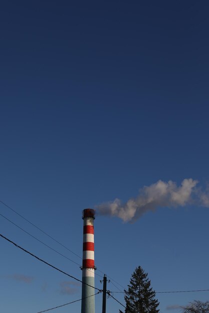 Red and white industrial chimney with smoke against blue sky background