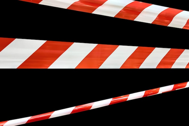 Red and white lines of barrier tape prohibit passage tape on\
black isolate background