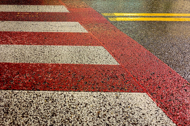 Red and white pedestrian crossing and yellow dividing strip on wet pavement