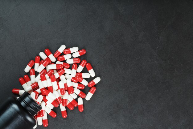 Red and white pills from a black jar on a black background. Free space