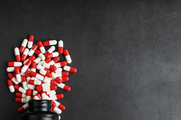 Red and white pills from a black jar on a black background.